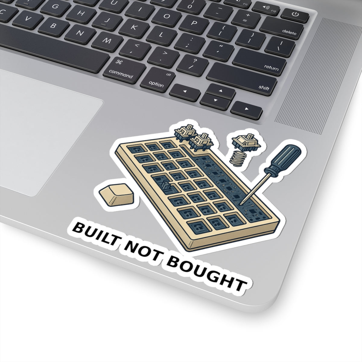 Mechanical keyboard sticker with “Built Not Bought” design shown on a silver MacBook — featuring switch tools and keycaps for modders and builders.
